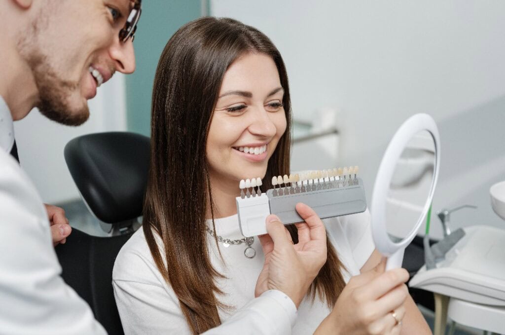 Junger Mann Zahnarzt im weißen Kittel zeigen Veneers Schmelz Farbpalette für schöne Patientin Frau